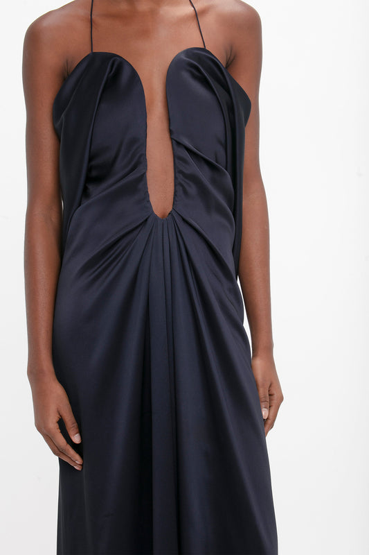 Woman wearing an elegant navy blue evening gown with a plunging neckline and gathered waist, focusing on the upper part of the Victoria Beckham Frame Detail Cut-Out Cami Dress In Navy.