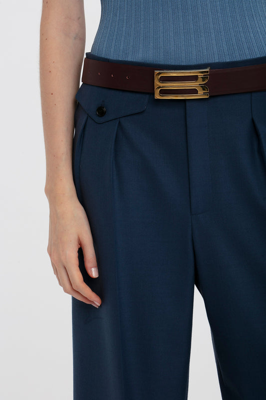 Close-up of a woman's side, showing a hand resting on her hip, wearing Victoria Beckham wide leg cropped trousers in heritage blue made from recycled wool with a brown belt.