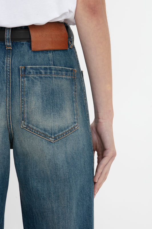 Close-up of a person wearing Victoria Beckham's Alina Jean In Indigrey Wash, showing a back pocket and a brown leather belt with a label. The hand is resting on the hip.
