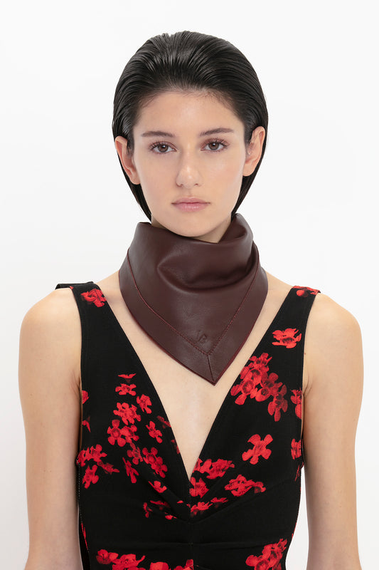 A woman with slicked-back hair wearing a floral dress and a Victoria Beckham Foulard In Bordeaux Leather, posing against a white background.