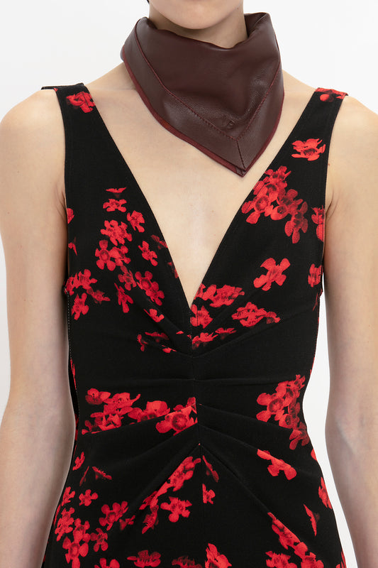 Woman wearing a black dress with red floral patterns and a Victoria Beckham Foulard In Bordeaux Leather neck scarf, close-up view of neckline and scarf.