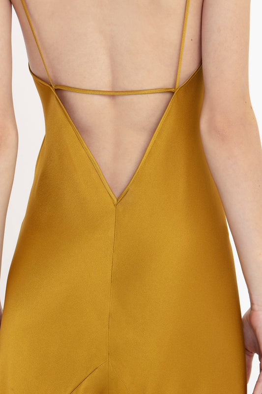 Close-up of the back of a woman wearing a Victoria Beckham Low Back Cami Floor-Length Dress In Harvest Gold with a criss-cross strap design.