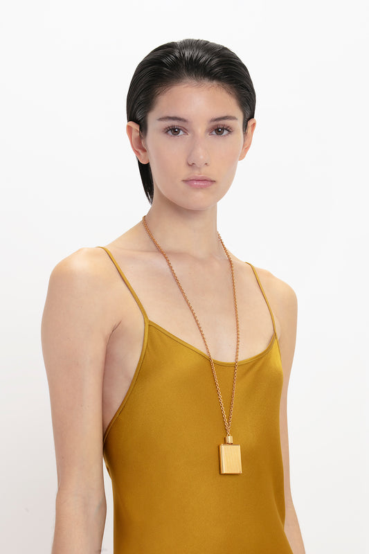 Woman in a Victoria Beckham Low Back Cami Floor-Length Dress In Harvest Gold with a long gold necklace, looking directly at the camera against a white background.