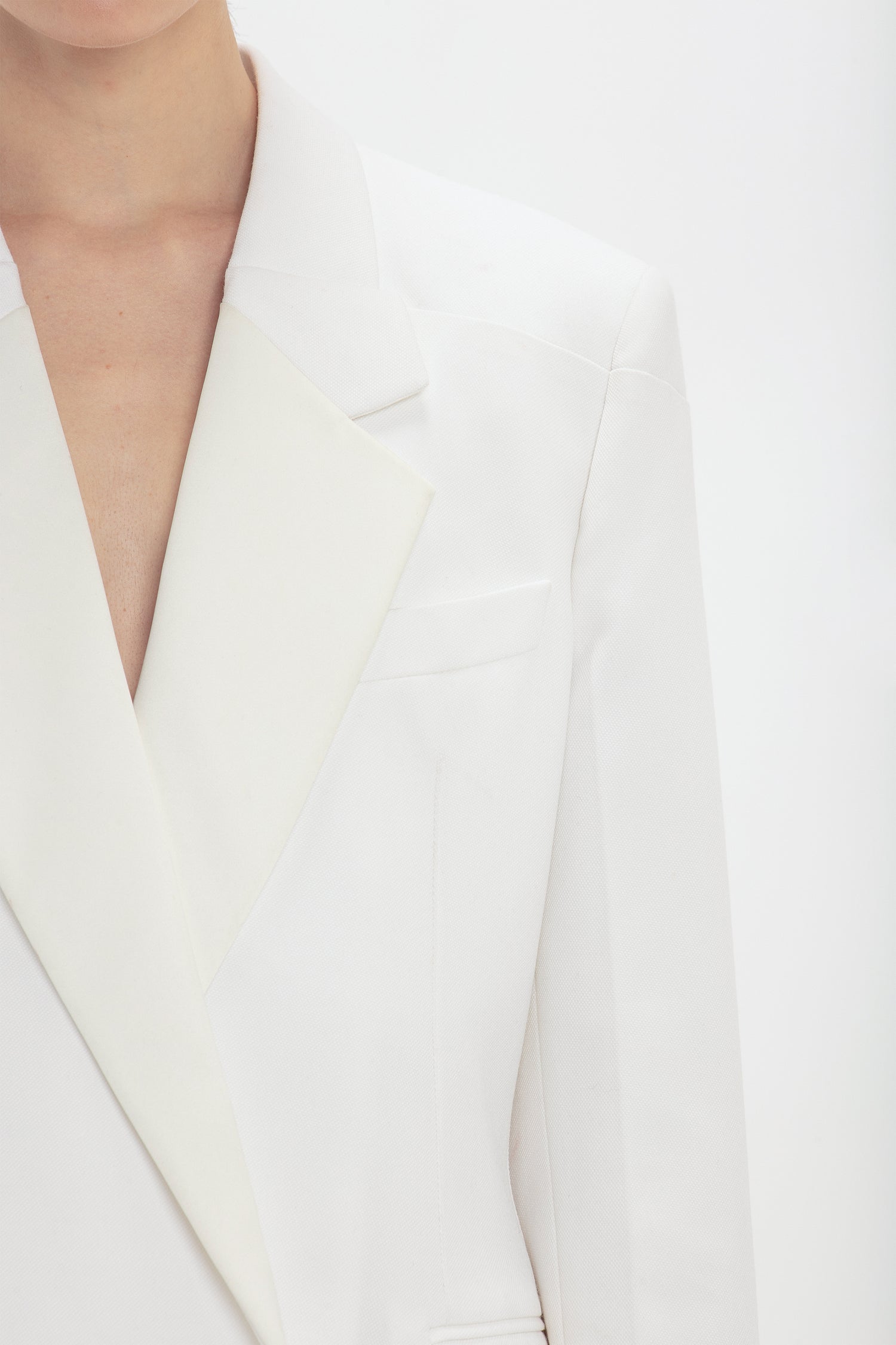 Close-up of a person wearing a Victoria Beckham Exclusive Fold Shoulder Detail Dress In Ivory, focusing on the upper chest and neck area.