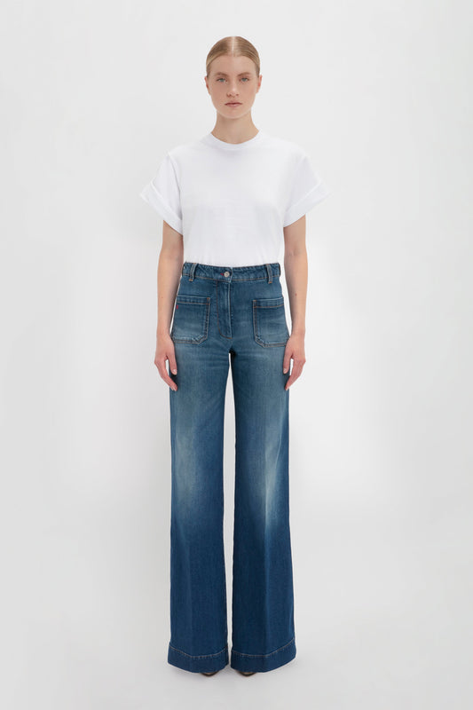 A woman standing in front of a white background, wearing an oversized Victoria Beckham Asymmetric Relaxed Fit T-Shirt in White and high-waisted Alina Jean in Dark Vintage Wash.
