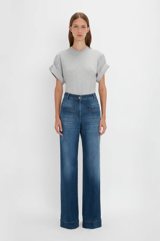 A woman standing against a white background wearing an Asymmetric Relaxed Fit T-Shirt in Grey Marl and blue high-waisted jeans from Victoria Beckham.