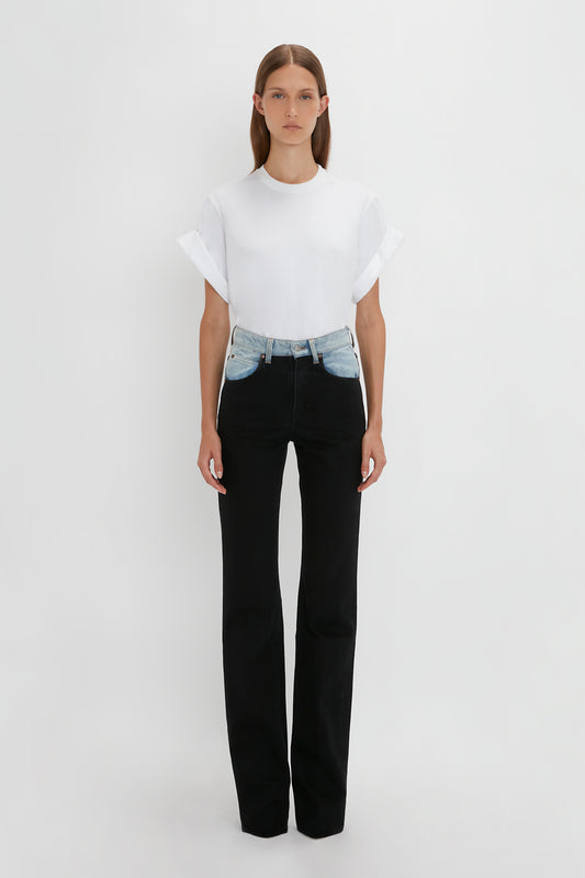 A woman wearing a white t-shirt and Victoria Beckham Julia Jean In Contrast Wash denim high waist jeans stands against a plain white background.