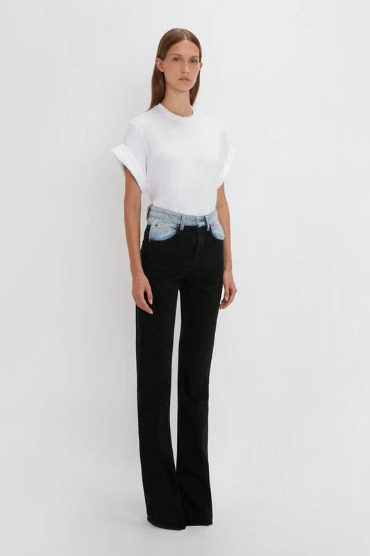 A woman in a white t-shirt and black high waist jeans with a Victoria Beckham Julia Jean In Contrast Wash denim belt, standing against a plain white background.