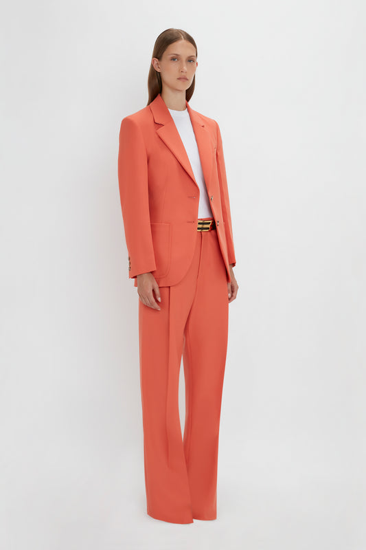 A woman in a stylish Victoria Beckham Patch Pocket Jacket In Papaya pantsuit with a white top, standing against a white background.