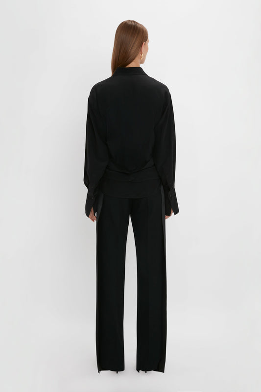 Woman posing from behind wearing a Victoria Beckham Wrap Front Blouse In Black and oversized fit trousers against a white background.