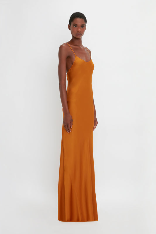 A black woman modeling a floor-length cami dress in ginger by Victoria Beckham against a plain white background.