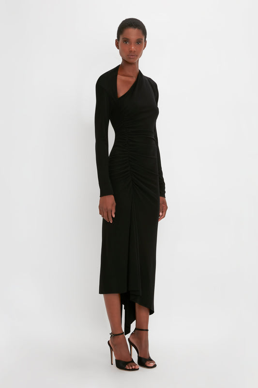 A woman in a Victoria Beckham Slash-Neck Ruched Midi Dress In Black and high heels posing against a plain white background.