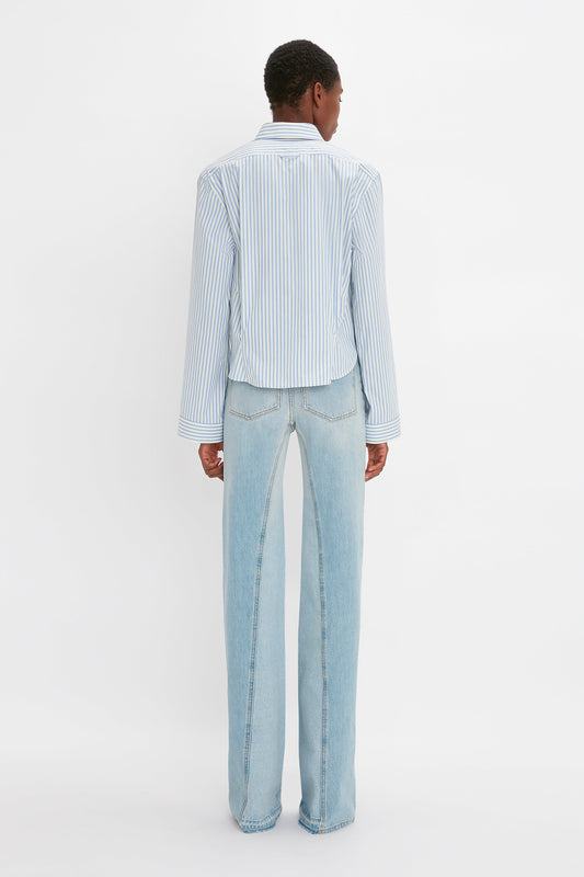 A man seen from the back wearing a vertically striped blue and white Button Detail Cropped Shirt and Victoria Beckham's Bianca Jean In Light Blue Denim, standing against a plain white background.