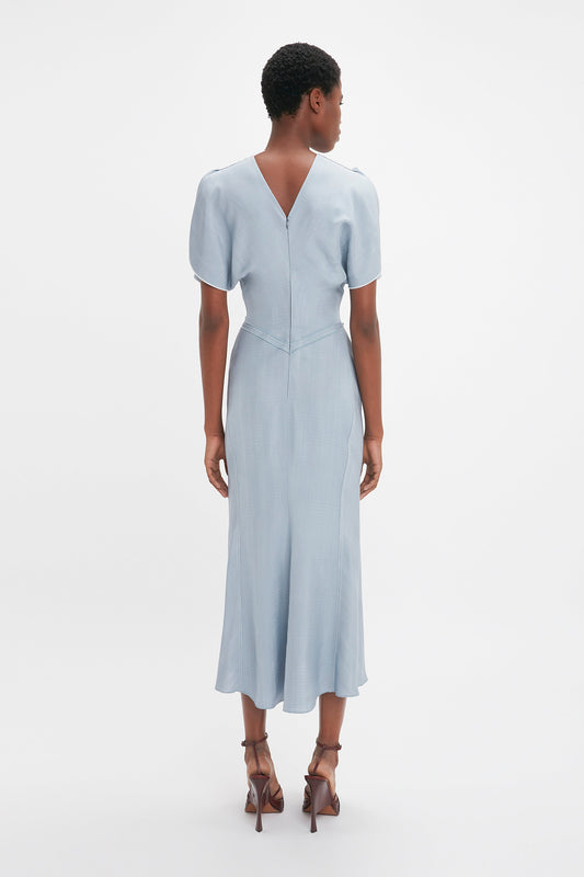 A woman viewed from behind, wearing a light blue Exclusive Gathered Waist Midi Dress In Pebble by Victoria Beckham and brown heels, standing against a white background.
