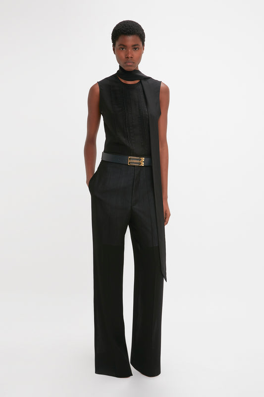 A black woman models a modern Victoria Beckham black sleeveless top and Victoria Beckham high-waisted, straight-leg trousers with a belt, standing against a white backdrop.
