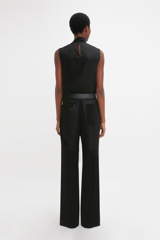 Rear view of a person wearing Victoria Beckham's Waistband Detail Straight Leg Trouser In Black and a modern black sleeveless top, against a plain white background.