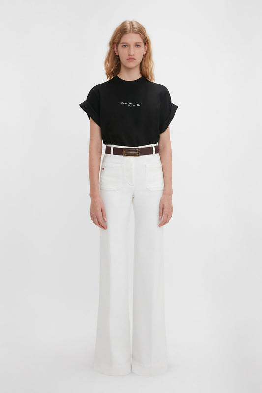 Young woman wearing a Victoria Beckham 'Do As I Say, Not As I Do' Slogan T-shirt in black and white high-waisted flared jeans, standing against a plain white background.