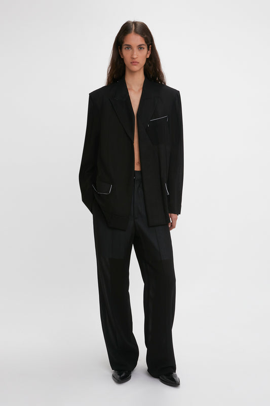 A woman models a Victoria Beckham black suit featuring a Fold Detail Tailored Jacket and straight leg trousers with waistband detail, standing against a plain white background.