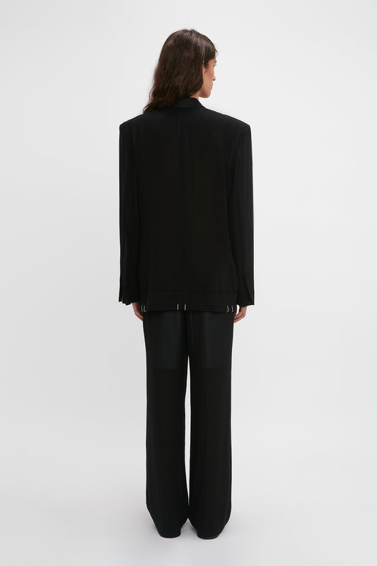 A woman in a chic Victoria Beckham Fold Detail Tailored Jacket in Black standing with her back to the camera against a white background.