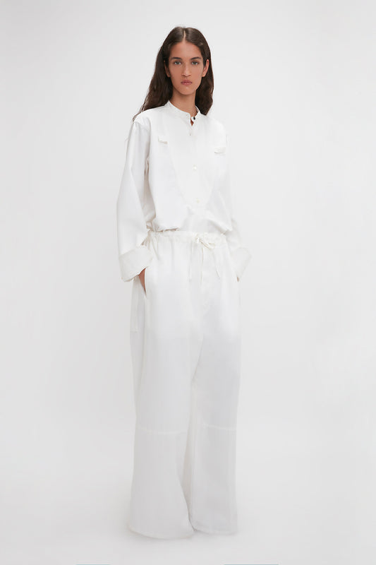 A woman in Victoria Beckham's chic Drawstring Pyjama Trouser In Washed White with an adjustable drawstring waistband, standing against a plain light background.