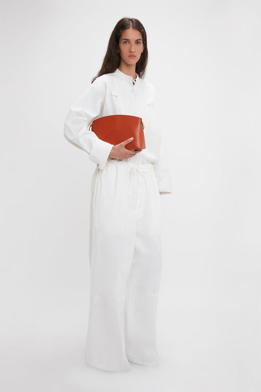 A woman in Victoria Beckham's Drawstring Pyjama Trouser In Washed White holds a red handbag, standing against a plain background.