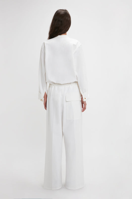 Woman viewed from behind wearing a Victoria Beckham Drawstring Pyjama Trouser In Washed White with a blouse and wide-leg trousers, standing against a plain background.