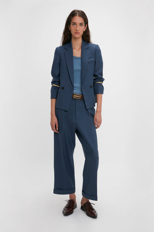 A woman in a professional Victoria Beckham Shrunken Double Breasted Jacket In Heritage Blue pantsuit and brown shoes stands confidently against a white background.