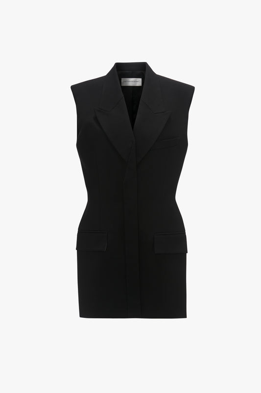 Sleeveless tailored dress in black vest, crafted from a recycled wool blend, with notched lapels and front pockets on a white background by Victoria Beckham.