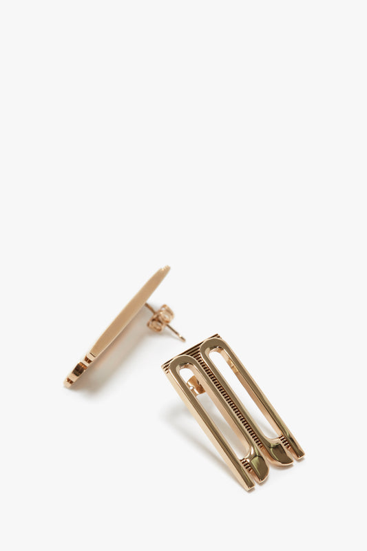 Two Victoria Beckham gold-plated brass hair clips on a white background, one open and one partially closed.