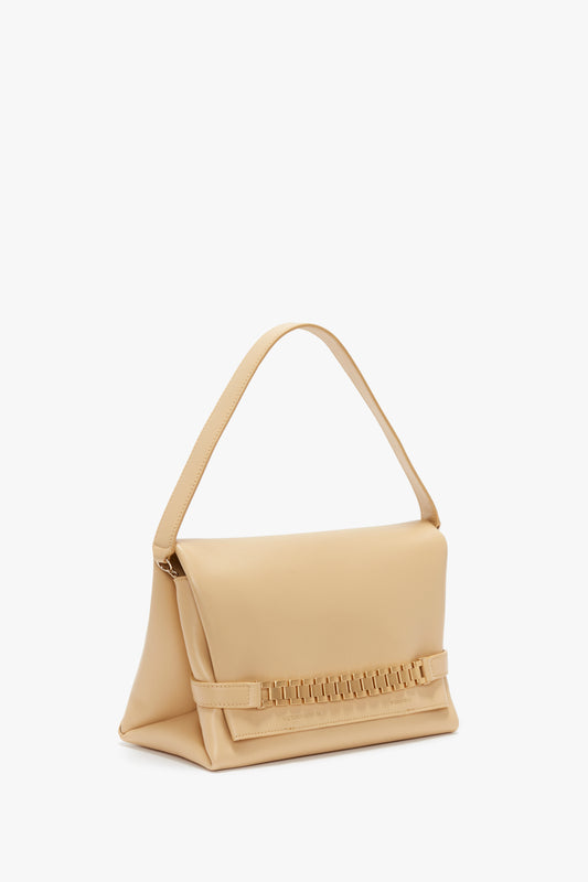 Beige leather crossbody bag with a fold-over top and gold chain detail on a white background. 
Chain Pouch With Strap In Sesame Leather by Victoria Beckham.