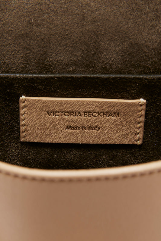 Close-up of a Victoria Beckham Mini Pouch With Long Strap In Sesame Leather brand label on a tan leather mini pouch handbag, stating "Made in Italy.