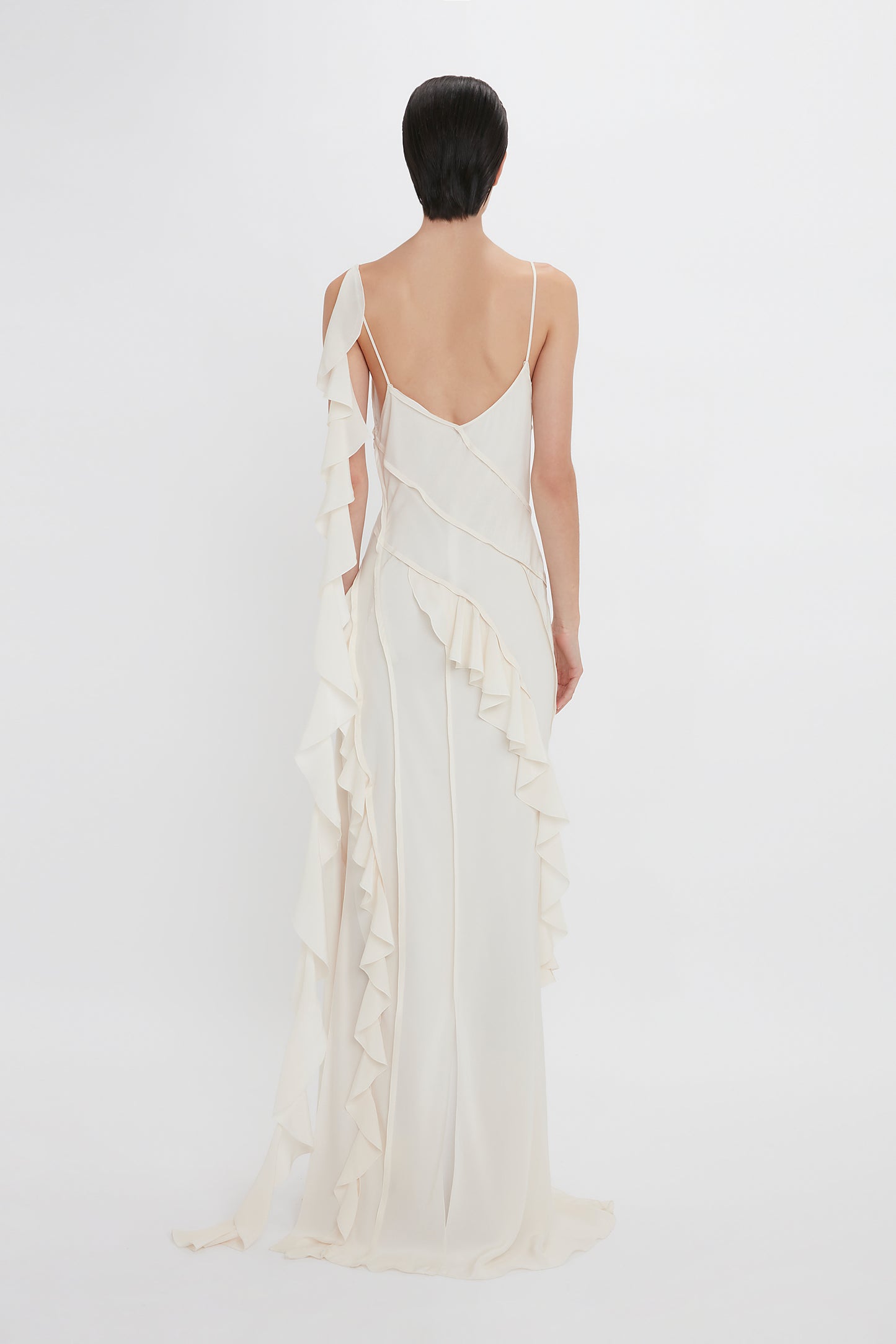 Woman in an elegant Victoria Beckham Exclusive Asymmetric Bias Frill Dress In Ivory with ruffled detailing, viewed from behind against a plain background.