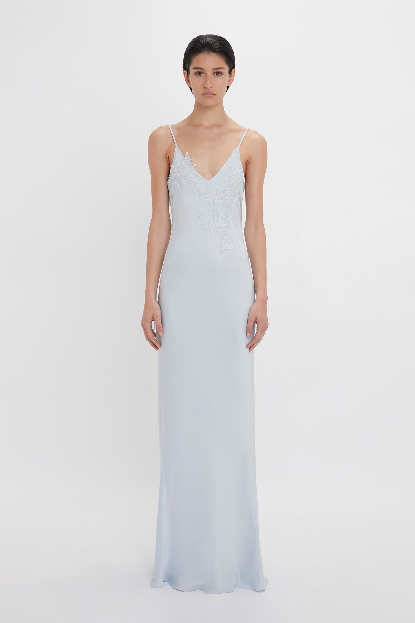 A woman in a Victoria Beckham Exclusive Lace Detail Floor-Length Cami Dress In Ice, standing against a white background.