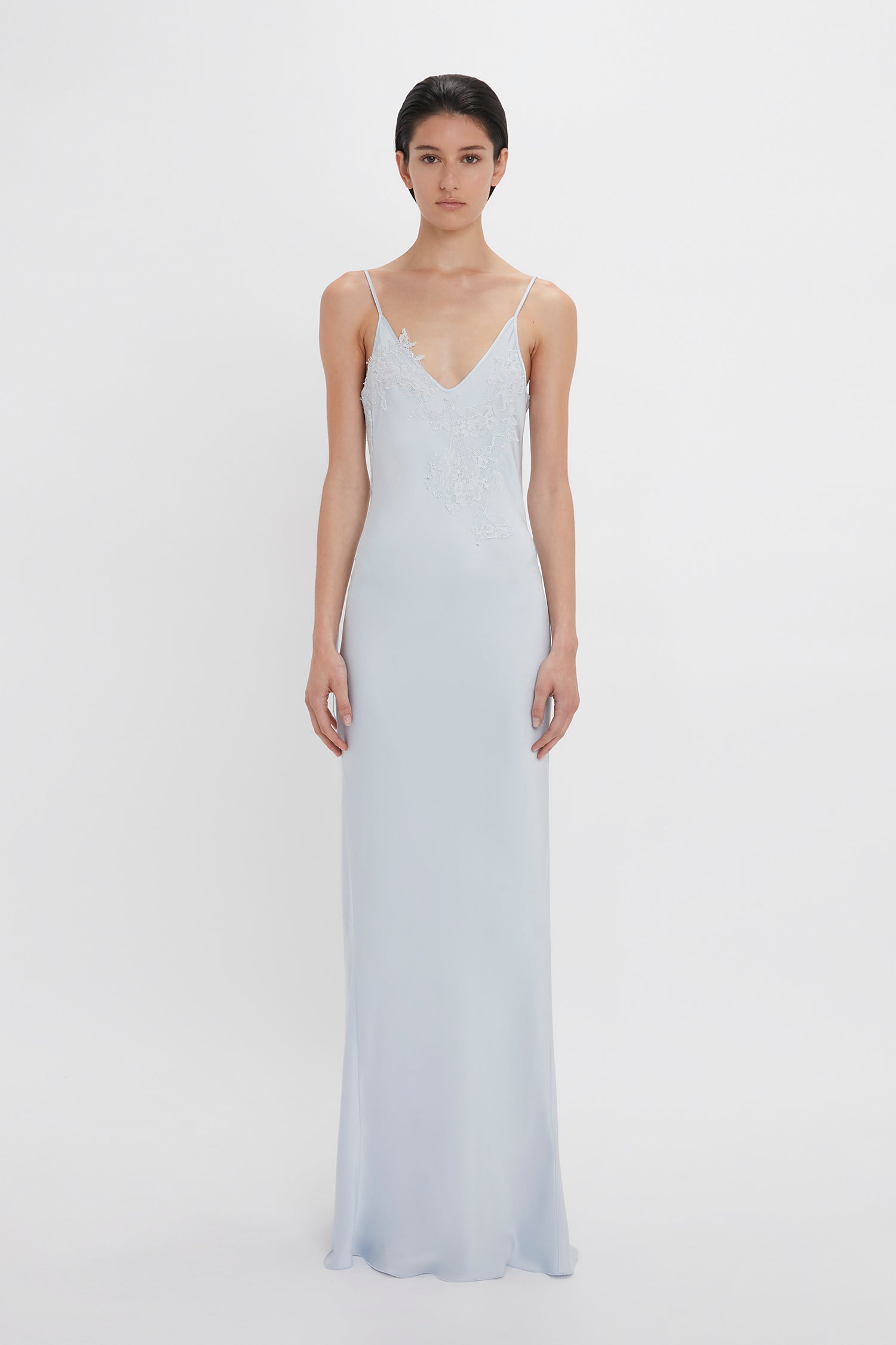 A woman in a Victoria Beckham Exclusive Lace Detail Floor-Length Cami Dress In Ice, standing against a white background.