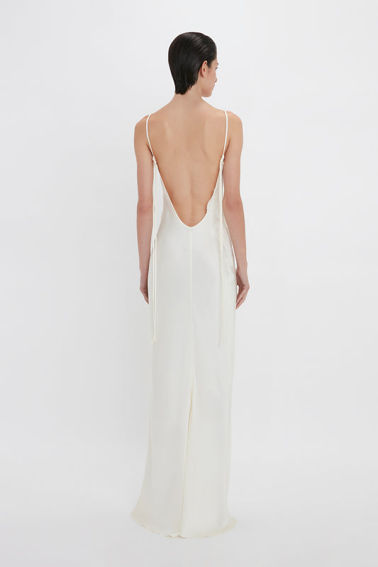 A woman viewed from behind wearing a sleeveless white satin Victoria Beckham dress with a low-cut back and delicate straps.