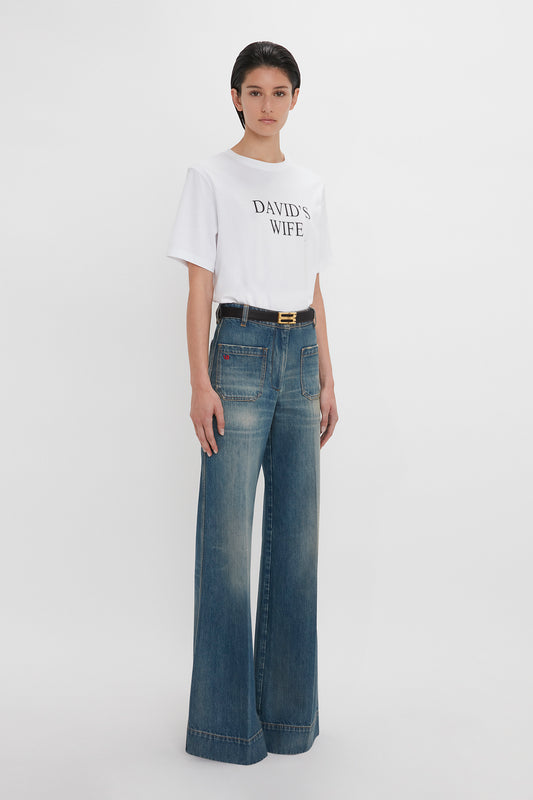 Woman in a white t-shirt with "David's wife" text and Alina Jean In Indigrey Wash by Victoria Beckham, standing against a plain white background.