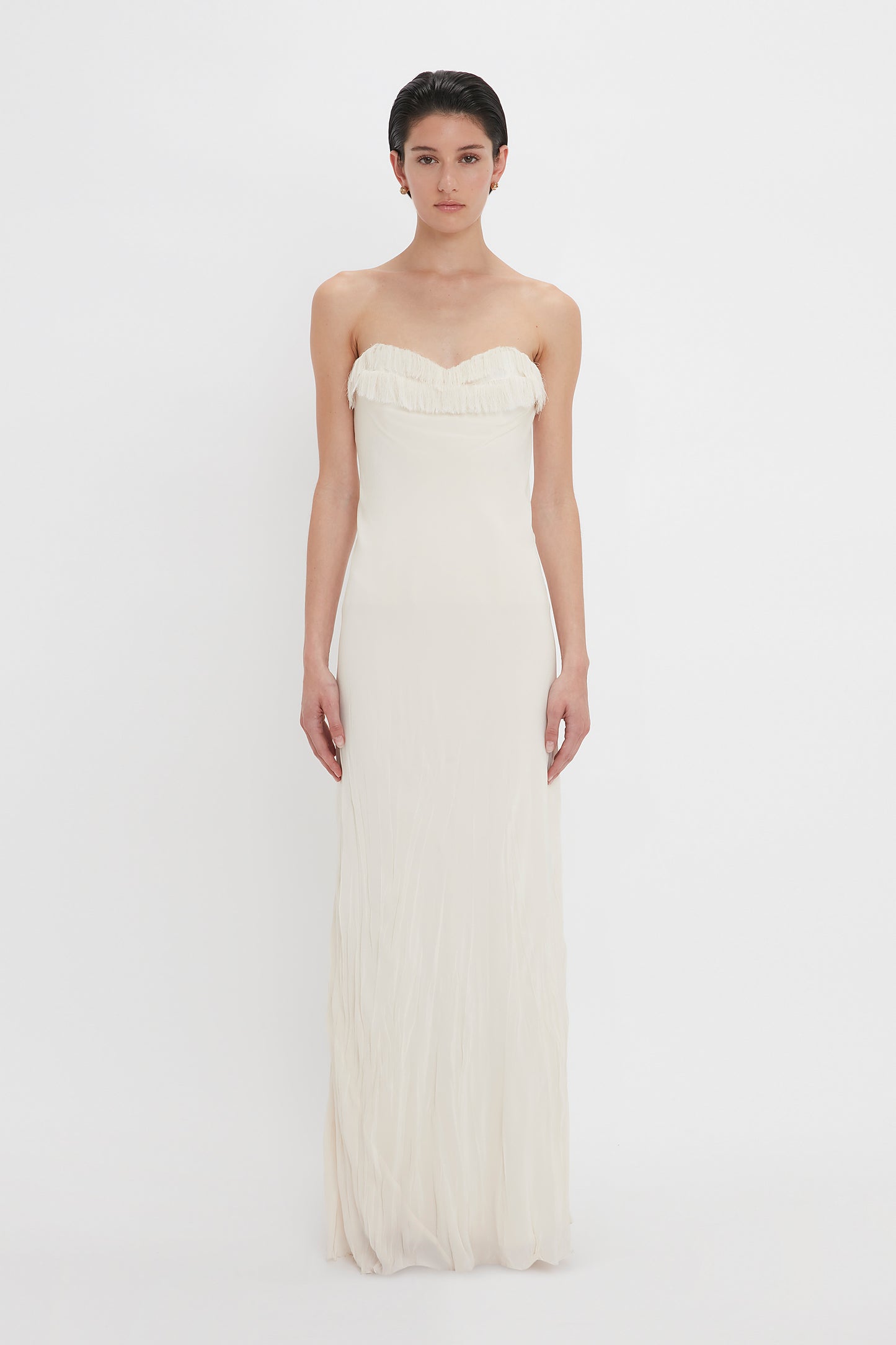 A woman in a strapless Victoria Beckham Exclusive Floor-Length Corset Detail Gown In Ivory stands against a plain white background, looking directly at the camera.