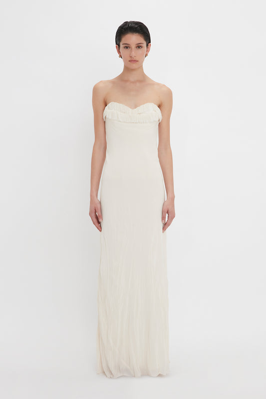A woman in a strapless Victoria Beckham Exclusive Floor-Length Corset Detail Gown In Ivory stands against a plain white background, looking directly at the camera.