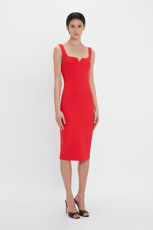 A woman in a red sleeveless fitted T-shirt dress in bright red with a sweetheart neckline, standing against a white background by Victoria Beckham.