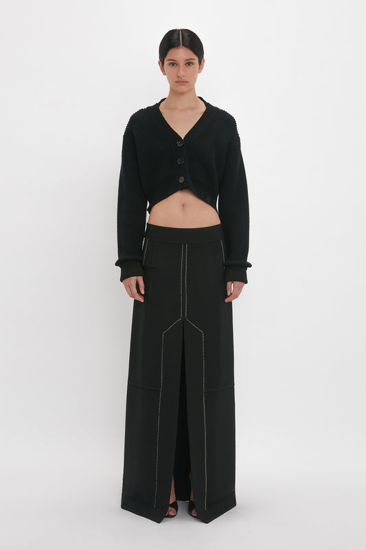 A woman models a black Cropped V-Neck Cardigan In Black with a Victoria Beckham monogram and high-waisted wide-leg trousers with white stitching while standing against a white background.