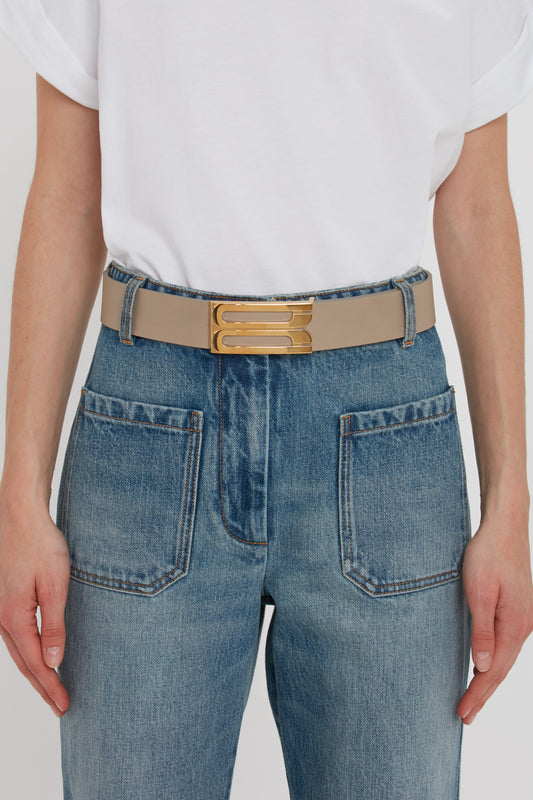 Woman wearing blue jeans with a Exclusive Jumbo Frame Belt In Beige Leather made of calf leather, focusing on her midsection against a plain white background.