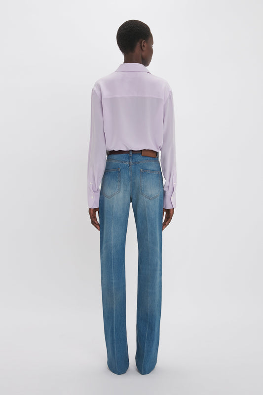 Rear view of a person wearing a Victoria Beckham asymmetric ruffle blouse in petunia and blue jeans, standing against a white background.