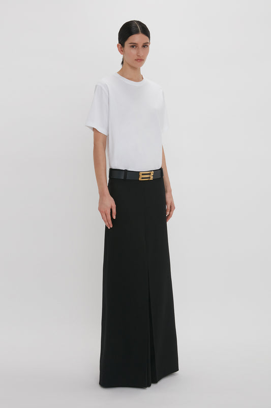 A woman in a stylish outfit consisting of an organic cotton Victoria Beckham Tee and black wide-leg pants with a prominent gold buckle belt.