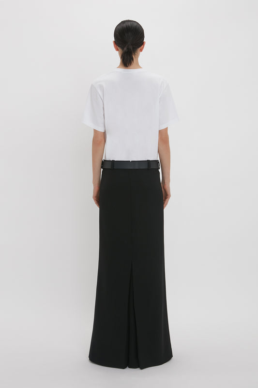 Woman from behind wearing a white Victoria Beckham Tee and black wide-leg trousers, standing against a plain white background.