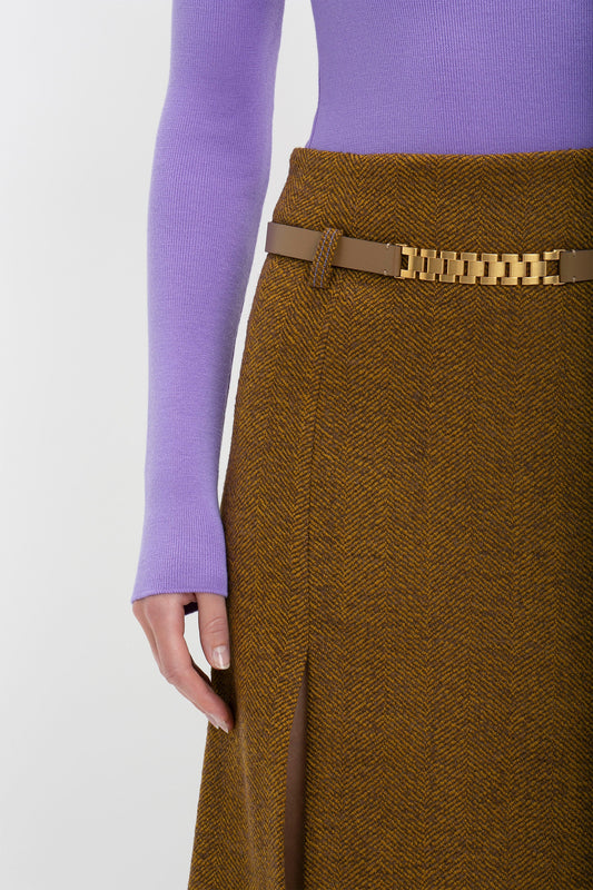 Woman wearing a purple sweater and brown tweed skirt with a Victoria Beckham calf-leather watch strap detail belt in khaki-brown, only showing from the waist to the thighs.