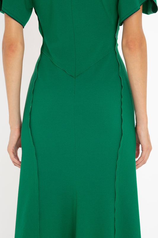 A close-up of a woman wearing a green Gathered V-Neck Midi Dress in Emerald with scalloped edges and a tailored waist by Victoria Beckham.
