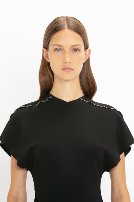 Woman with straight brown hair wearing a Victoria Beckham Short Sleeve Tie Detail Dress in Black, standing against a white background.