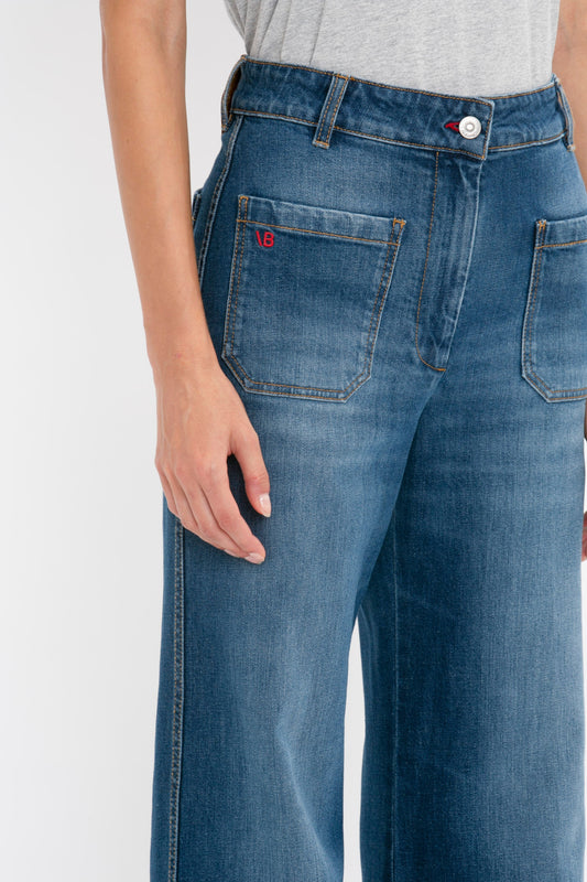 Close-up of a person wearing Victoria Beckham's Alina Jean in Dark Vintage Wash, focusing on the side pocket with a small red logo, hand gently resting on the thigh.