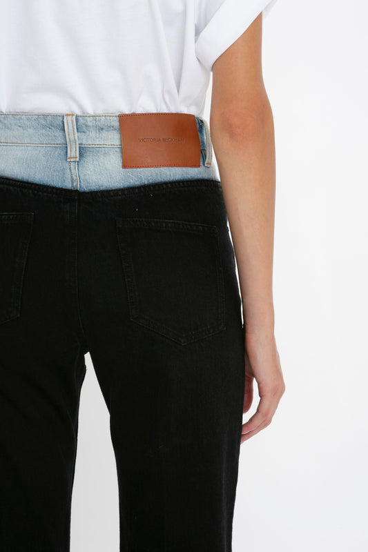 Woman wearing Victoria Beckham high waist black Julia Jeans In Contrast Wash with a white t-shirt tucked in, showcasing a leather brand patch on the back waistband.