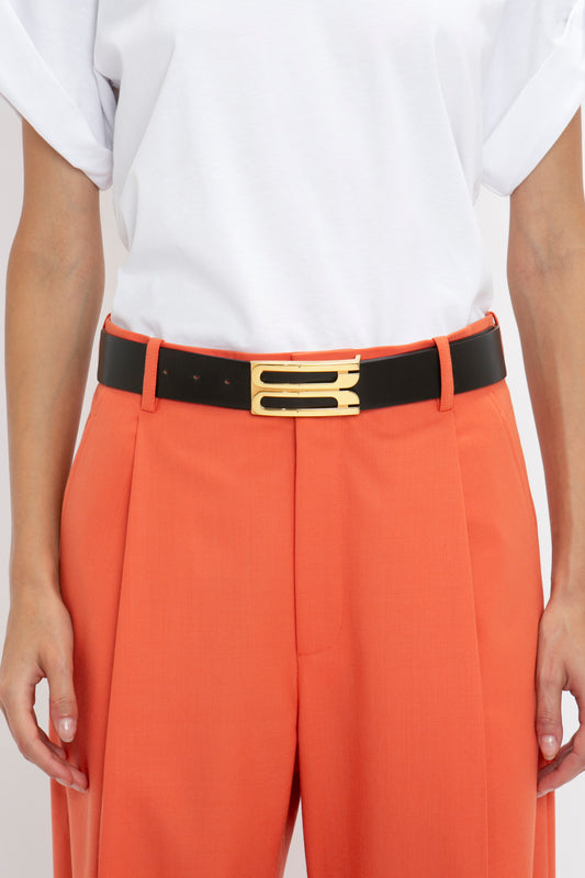 Close-up of a person wearing a white shirt tucked into orange trousers with a Victoria Beckham Exclusive Jumbo Frame Belt In Black Leather featuring gold hardware.